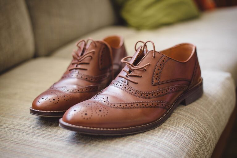 Une paire de chaussures de ville en cuir marron posée sur un canapé clair
